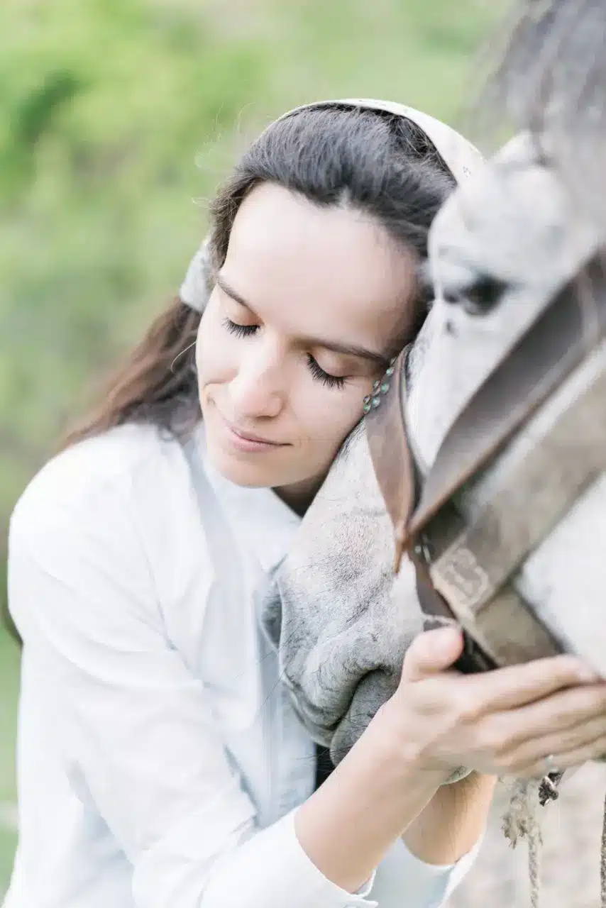 girl cups a horse's face in her hands and leans her head against it with her eyes closed during equine therapy